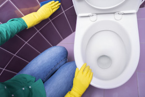 Hands in yellow gloves washing a toilet bowl.
