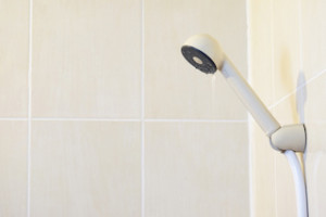 cream color plastic shower head (Selected focus) with little water flowing hang on hanger on the cream color tiles wall